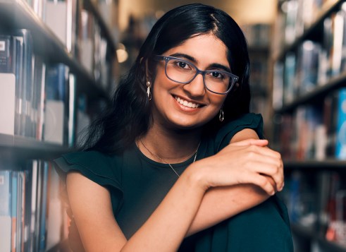 A smiling teenage girl wearing glasses, sitting in a library