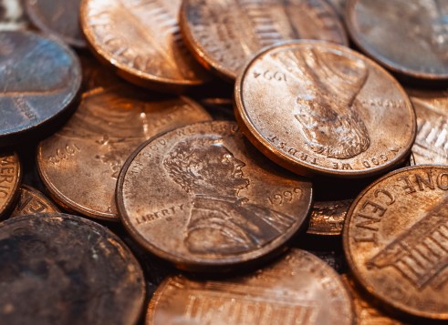 Close-up of a pile of shiny copper pennies, showing the heads and tails of U.S. one-cent coins.