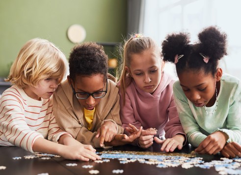 A group of four kids sitting at a table working on a jigsaw puzzle together