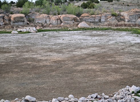 Dry resevoir surrounded by rocks and dry brush in a desert landscape.