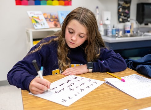 A girl sits at a desk, practicing handwriting.