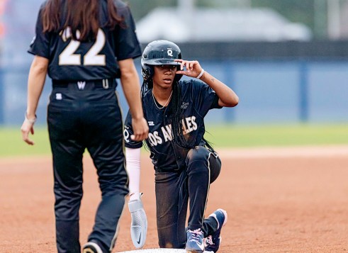 A young baseball player wearing a helmet kneels on a base.